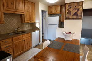 Kitchen with white appliances, a sink, backsplash, brown cabinets, and dark stone countertops