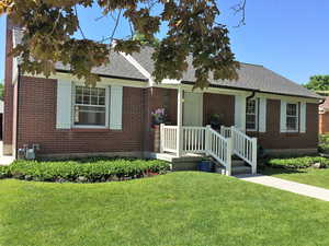 View of front of home with brick siding, roof with shingles, and a front lawn
