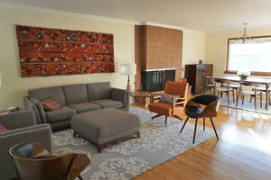 Living room featuring wood finished floors, crown molding, and a brick fireplace