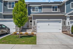View of property with stone siding, a shingled roof, concrete driveway, and a garage