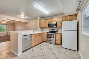 Kitchen with stainless steel appliances, a sink, light brown cabinetry, a peninsula, and light tile patterned flooring