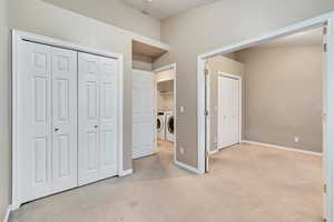 Unfurnished bedroom with washing machine and dryer, light carpet, and baseboards