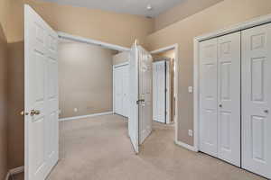 Unfurnished bedroom with multiple closets, light carpet, and baseboards
