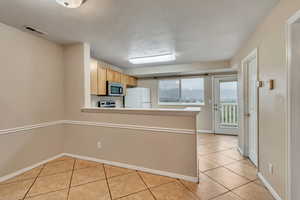 Kitchen featuring freestanding refrigerator, stainless steel microwave, light tile patterned flooring, and a peninsula