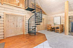 Interior space with spiral stairway, a high vaulted ceiling, a stone fireplace, and log walls