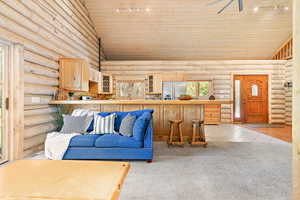 Living room with rail lighting, wooden ceiling, log walls, and high vaulted ceiling