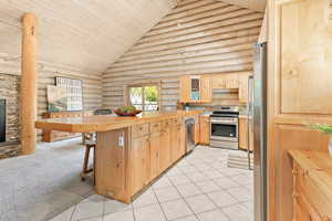 Kitchen featuring light cabinetry, wooden ceiling, rustic walls, a peninsula, and updated stainless steel appliances