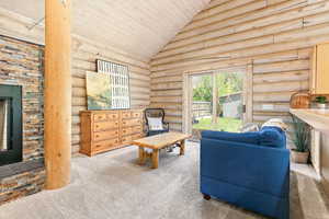 Carpeted living area with soaring vaulted ceiling, log walls, and sliding glass doors leading to the brand new deck