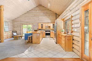Kitchen featuring light cabinetry, log walls, wood ceiling, high vaulted ceiling, and updated stainless steel appliances