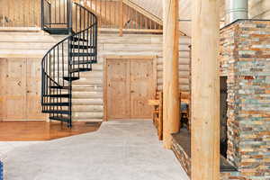 Spiral staircase, rustic walls, high vaulted ceiling, cedar beams, and stone gas fireplace