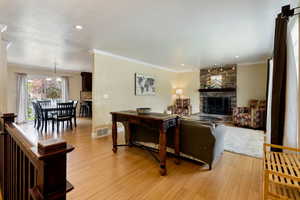 Living room with a fireplace, light wood-type flooring, crown molding, baseboards, and recessed lighting