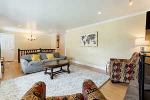 Living room with a chandelier, wood finished floors, ornamental molding, recessed lighting, and baseboards