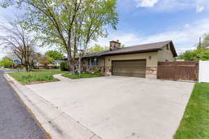 View of front of house featuring stone siding, a gate, a garage, concrete driveway, and a chimney