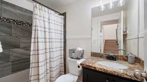 Bathroom with a wainscoted wall, vanity, shower / tub combo, toilet, and a textured ceiling