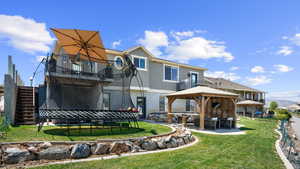 Rear view of house with a gazebo, a patio, a lawn, stucco siding, and stairs
