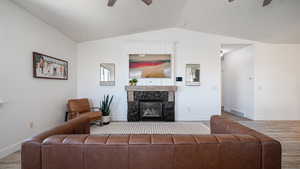 Living room featuring a ceiling fan, vaulted ceiling, wood finished floors, baseboards, and a fireplace