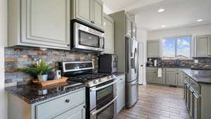 Kitchen with appliances with stainless steel finishes, gray cabinets, decorative backsplash, dark stone countertops, and recessed lighting