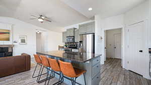 Kitchen with appliances with stainless steel finishes, light wood finished floors, ceiling fan, a kitchen bar, and vaulted ceiling