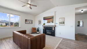 Living room featuring a ceiling fan, light wood-style flooring, lofted ceiling, a fireplace, and baseboards