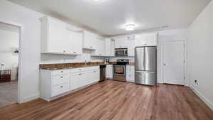Kitchen featuring stainless steel appliances, white cabinetry, baseboards, wood finished floors, and dark stone counters