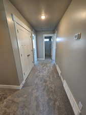 Hallway with carpet flooring, a textured ceiling, baseboards, and attic access