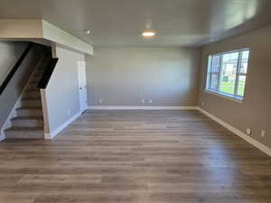 Unfurnished living room with stairway, baseboards, wood finished floors, recessed lighting, and a textured ceiling