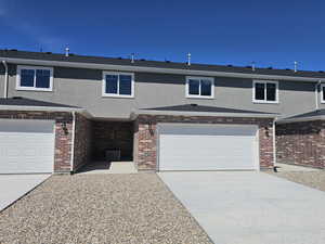 View of front of home featuring stucco siding, concrete driveway, a garage, and brick siding