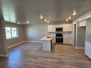 Kitchen with appliances with stainless steel finishes, a sink, a peninsula, light wood finished floors, and baseboards
