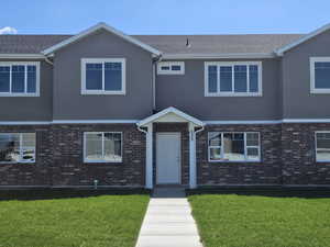 View of front facade with a front lawn, stucco siding, and brick siding