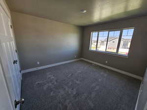 Spare room with dark colored carpet, baseboards, and a textured ceiling