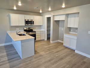 Kitchen featuring appliances with stainless steel finishes, a sink, baseboards, a peninsula, and white cabinetry