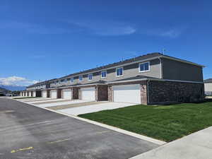 Townhome / multi-family property with stucco siding, a front yard, central AC unit, brick siding, and a garage