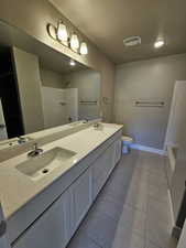 Bathroom featuring a shower, toilet, a textured ceiling, double vanity, and tile patterned floors