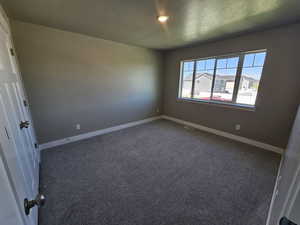Empty room with a textured ceiling, carpet flooring, and baseboards