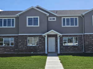 View of front of home featuring brick siding, a front yard, and stucco siding