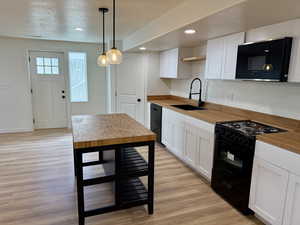 Kitchen with black appliances, white cabinets, light wood-style floors, decorative light fixtures, and recessed lighting