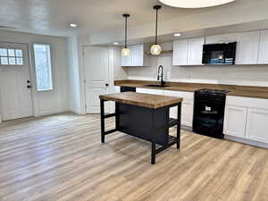 Kitchen featuring wood counters, a sink, black appliances, light wood-style floors, and open shelves