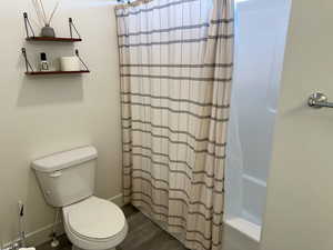 Full bathroom featuring toilet, wood finished floors, and shower / bath combination with curtain