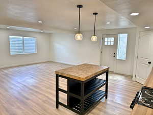 Kitchen with baseboards, black range with electric cooktop, light wood-type flooring, recessed lighting, and hanging light fixtures