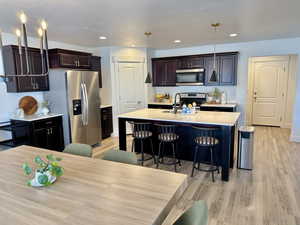 Kitchen featuring stainless steel appliances, a sink, light countertops, light wood-type flooring, and a kitchen breakfast bar