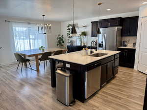 Kitchen with a sink, appliances with stainless steel finishes, a chandelier, light countertops, and light wood-type flooring