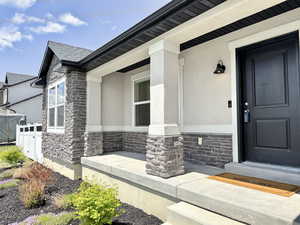 Entrance to property with stone siding, stucco siding, fence, and covered porch