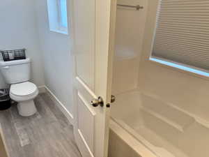 Full bath featuring toilet, a bathtub, baseboards, and wood finished floors