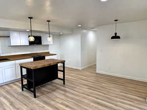 Kitchen with wood counters, black microwave, light wood-style floors, baseboards, and recessed lighting