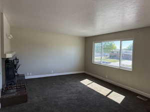 Unfurnished living room featuring a textured ceiling, dark colored carpet, a fireplace, and baseboards