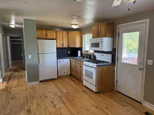 Kitchen with white appliances, dark countertops, a sink, and light wood-type flooring