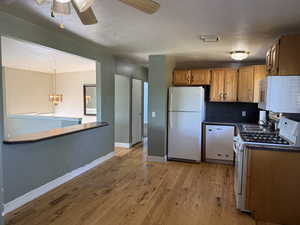 Kitchen featuring white appliances, dark countertops, light wood-style floors, a chandelier, and ceiling fan