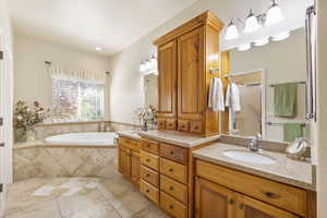 Primary bathroom featuring a jetted tub, double vanity, tile floors and solid cherry cabinets.