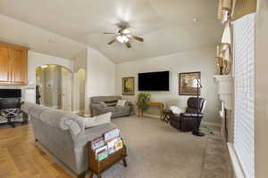Living room with a ceiling fan, lofted ceiling, a fireplace, baseboards, and arched walkways