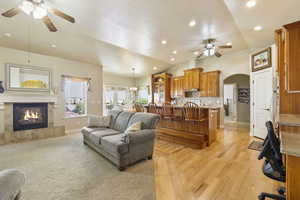 Living area with a fireplace, arched walkways, ceiling fan, baseboards, and vaulted ceiling